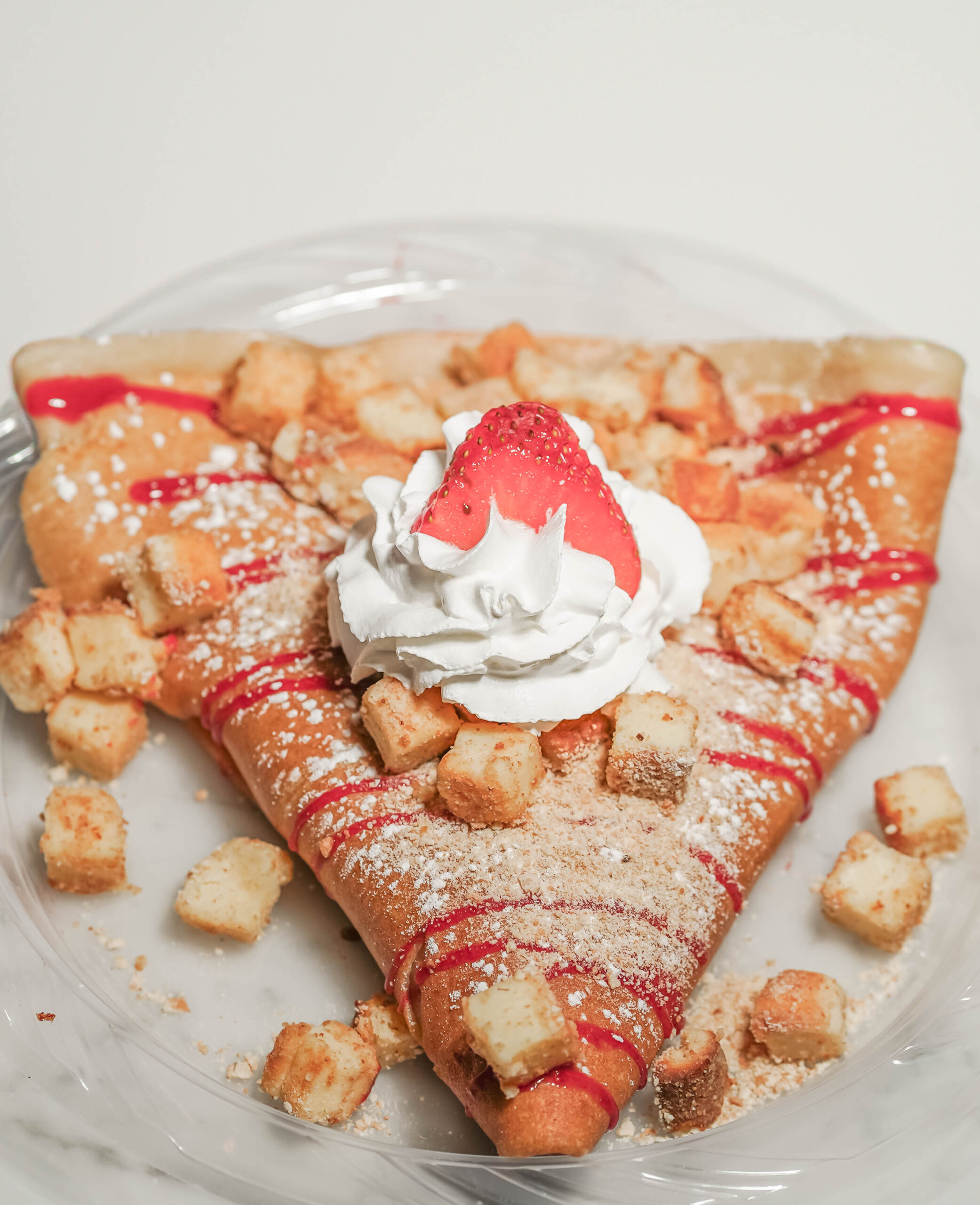 Strawberry cheesecake crepe with cheesecake bites, strawberry sauce, whipped cream and a fresh strawberry